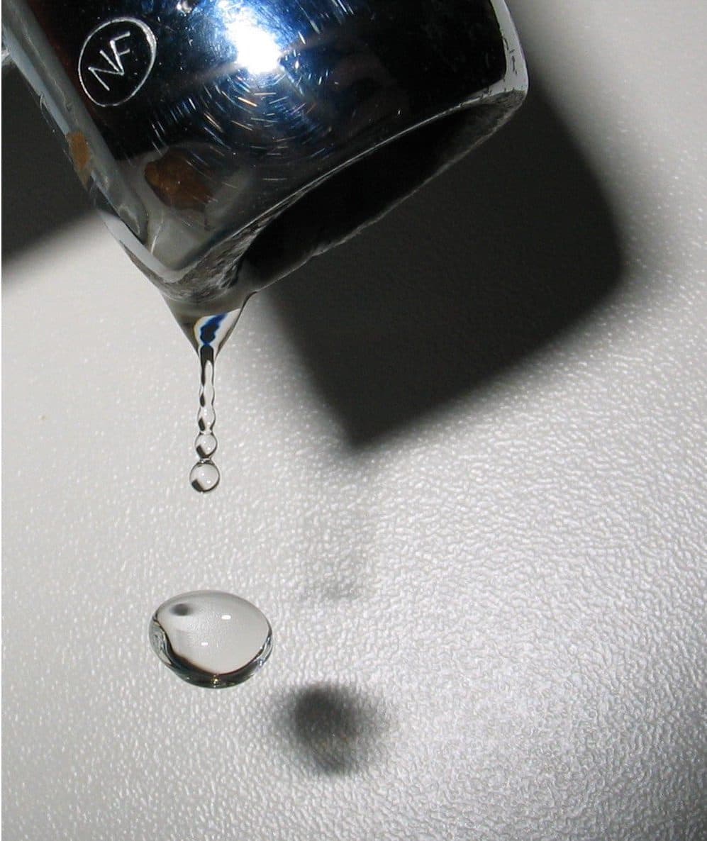A single drop detaching from the lip of a glass, in black and white